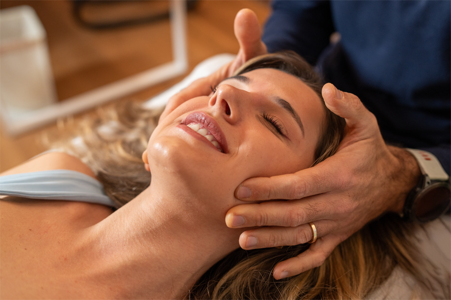 osteopata applica tecnica craniosacrale con mani ai lati della testa di una paziente sdraiata per trattare la cefalea